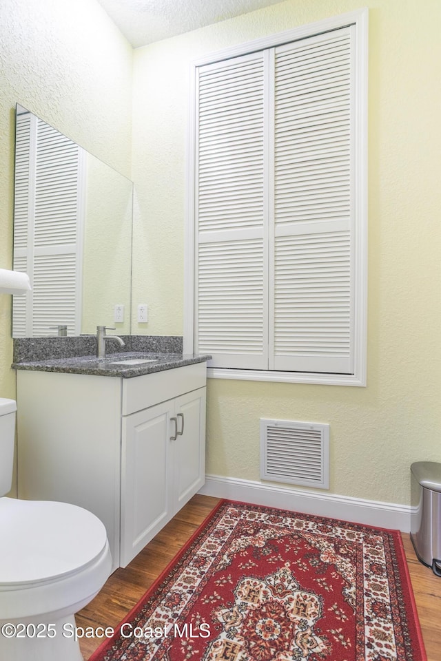 bathroom featuring visible vents, baseboards, wood finished floors, and toilet