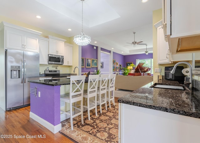 kitchen featuring wood finished floors, a raised ceiling, open floor plan, stainless steel appliances, and white cabinetry