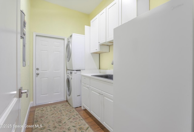 laundry room with stacked washer / drying machine, light wood-type flooring, and cabinet space