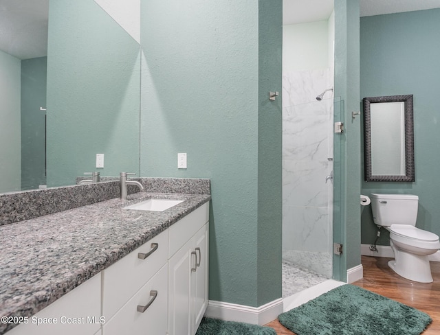 full bath with vanity, wood finished floors, toilet, baseboards, and a marble finish shower