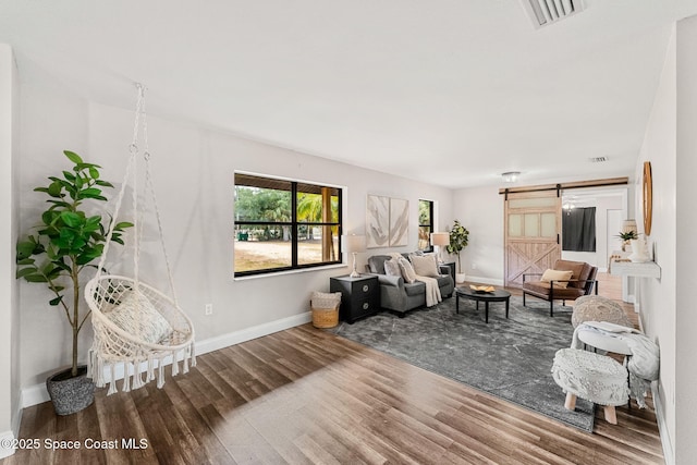 living room with visible vents, a barn door, baseboards, and wood finished floors