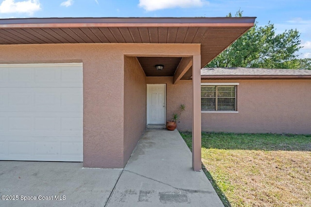 entrance to property with a lawn, an attached garage, and stucco siding
