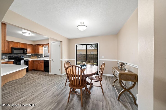 dining room with a textured ceiling, baseboards, and light wood-type flooring