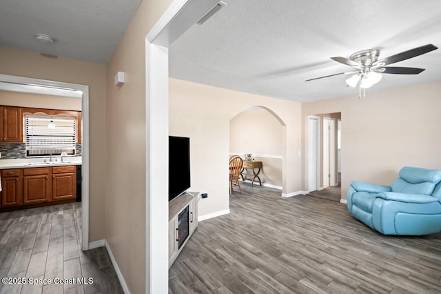 living area with ceiling fan, arched walkways, a textured ceiling, baseboards, and light wood-type flooring