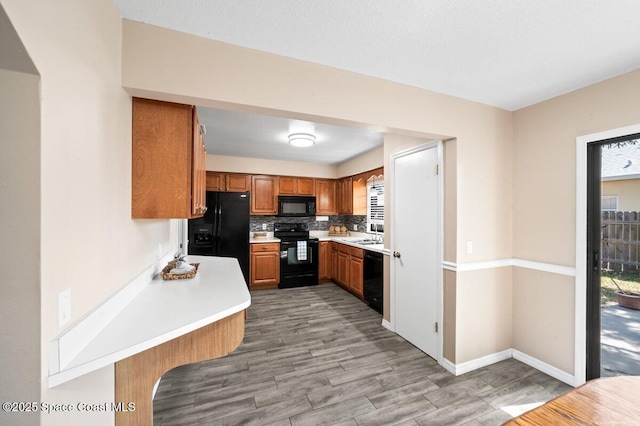 kitchen with light wood-style floors, light countertops, brown cabinets, backsplash, and black appliances