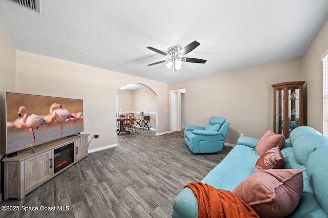 living area featuring arched walkways, a ceiling fan, baseboards, wood finished floors, and visible vents