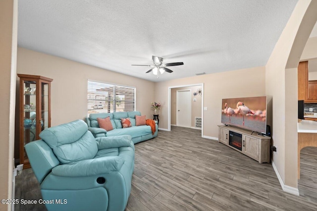 living area with a ceiling fan, a textured ceiling, arched walkways, baseboards, and light wood-style flooring
