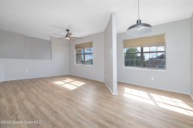 unfurnished living room with plenty of natural light, a ceiling fan, light wood-style floors, and baseboards