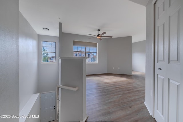 hallway with baseboards, wood finished floors, and an upstairs landing