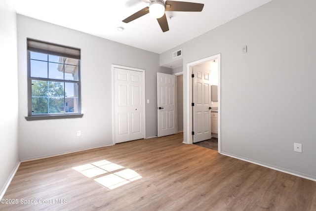 unfurnished bedroom with a ceiling fan, visible vents, wood finished floors, baseboards, and ensuite bathroom