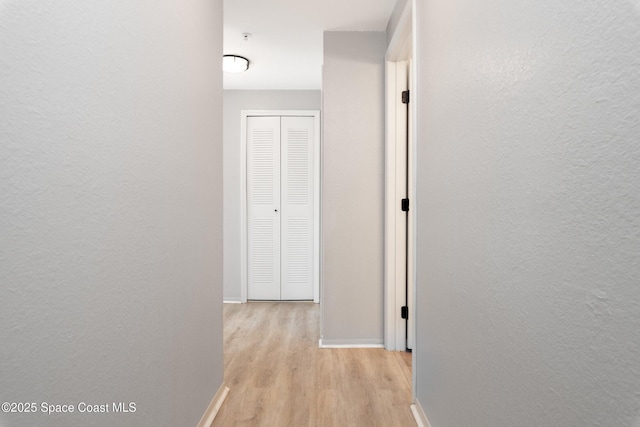 hallway with baseboards, a textured wall, and light wood-type flooring
