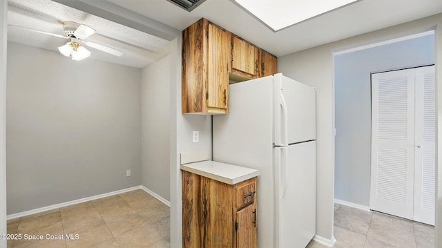 kitchen with ceiling fan, brown cabinetry, light countertops, baseboards, and freestanding refrigerator