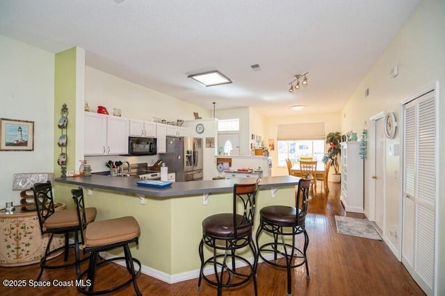 6190 Alderwood Ave, Cocoa, FL 32927 - kitchen featuring black microwave, dark countertops, dark wood-style floors, a peninsula, and stainless steel fridge