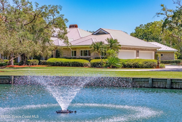 ranch-style home with an attached garage, a front lawn, brick siding, a standing seam roof, and metal roof
