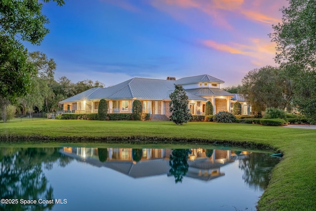 rear view of property featuring a water view, a yard, a chimney, and a standing seam roof
