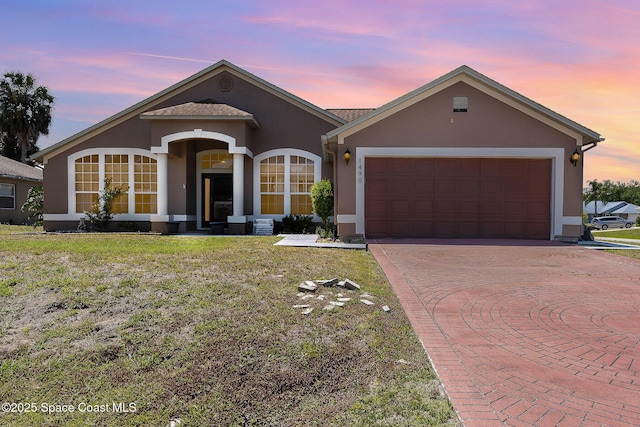 ranch-style home with a garage, curved driveway, stucco siding, and a front lawn