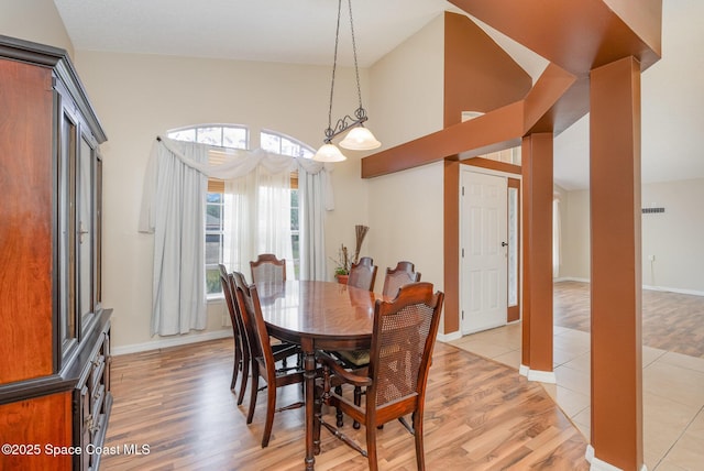 dining area with light wood-style floors, baseboards, and high vaulted ceiling