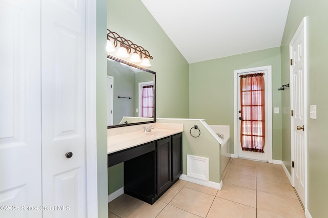 full bath with tile patterned flooring, a garden tub, vanity, lofted ceiling, and baseboards