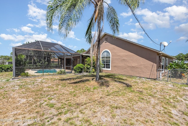 rear view of house with fence, stucco siding, an outdoor pool, a lawn, and a lanai