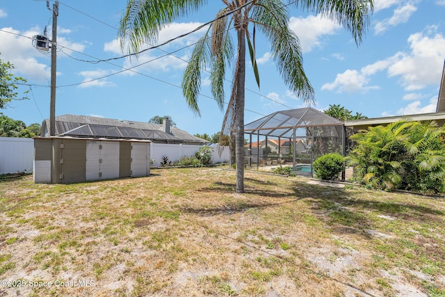 view of yard with a fenced backyard, a storage unit, an outdoor structure, and a lanai