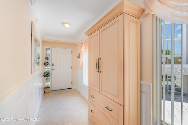 doorway featuring crown molding, wainscoting, a wealth of natural light, and a decorative wall