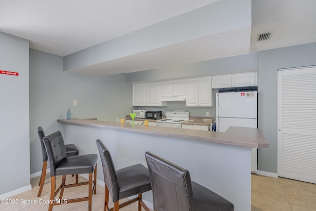 kitchen featuring visible vents, a peninsula, white appliances, a breakfast bar area, and under cabinet range hood