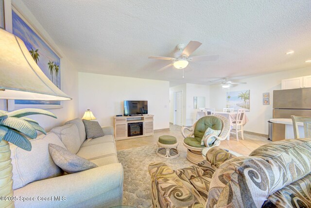 living area featuring a textured ceiling, a glass covered fireplace, a ceiling fan, recessed lighting, and light tile patterned floors