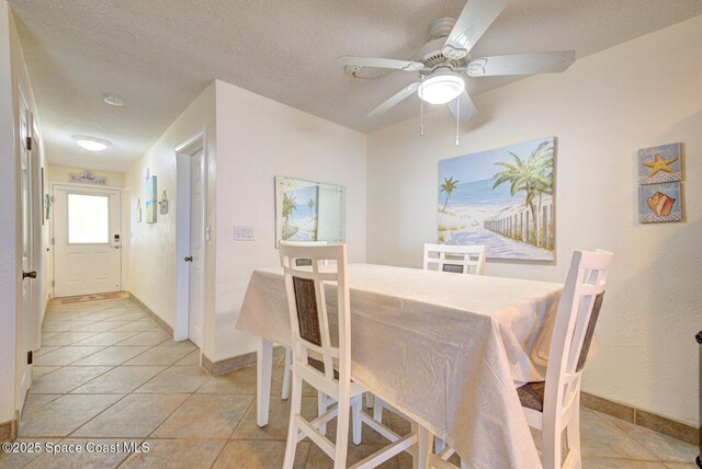 dining space featuring light tile patterned floors, baseboards, a ceiling fan, and a textured ceiling