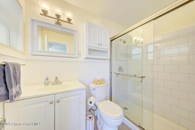 bathroom featuring vanity, a wainscoted wall, a stall shower, and toilet