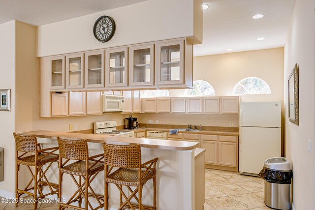 881 Glen Abbey Way, Melbourne, FL 32940 - kitchen featuring a peninsula, light brown cabinets, white appliances, a kitchen breakfast bar, and a sink