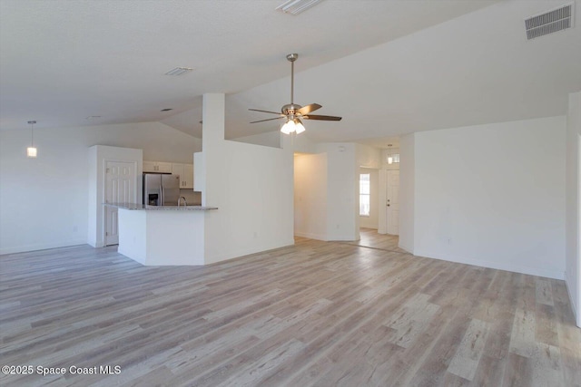 unfurnished living room with ceiling fan, visible vents, vaulted ceiling, baseboards, and light wood finished floors