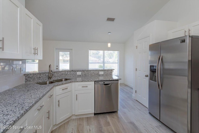 kitchen with a peninsula, lofted ceiling, white cabinets, a sink, and stainless steel appliances