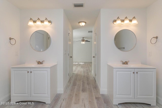 bathroom featuring visible vents, wood finished floors, baseboards, ceiling fan, and two vanities
