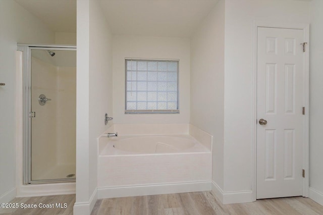 full bathroom featuring baseboards, wood finished floors, a bath, and a stall shower