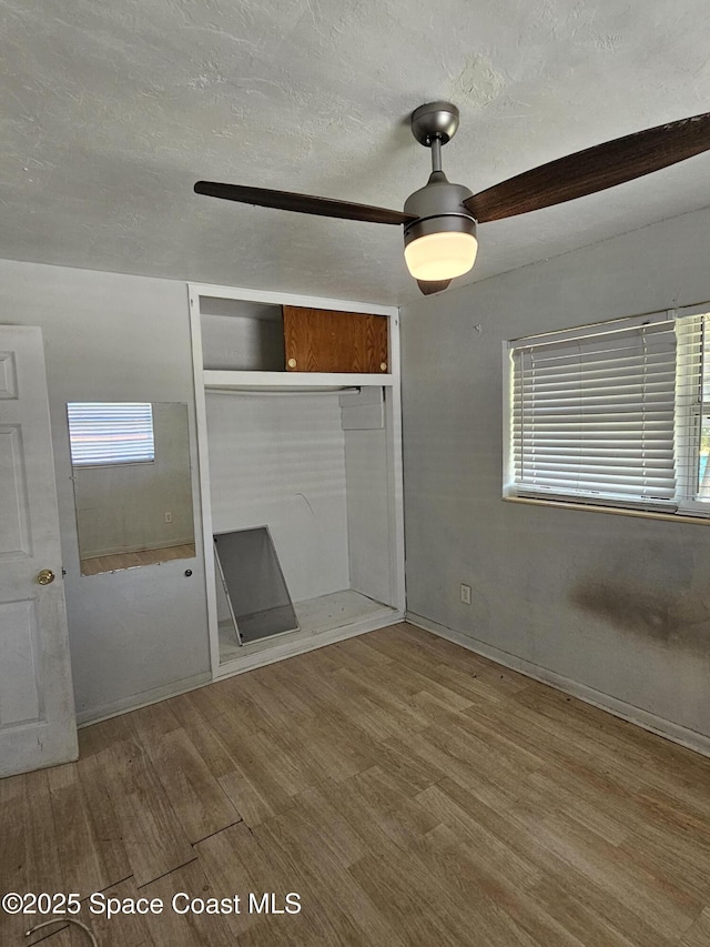unfurnished bedroom featuring ceiling fan, multiple windows, wood finished floors, and a closet
