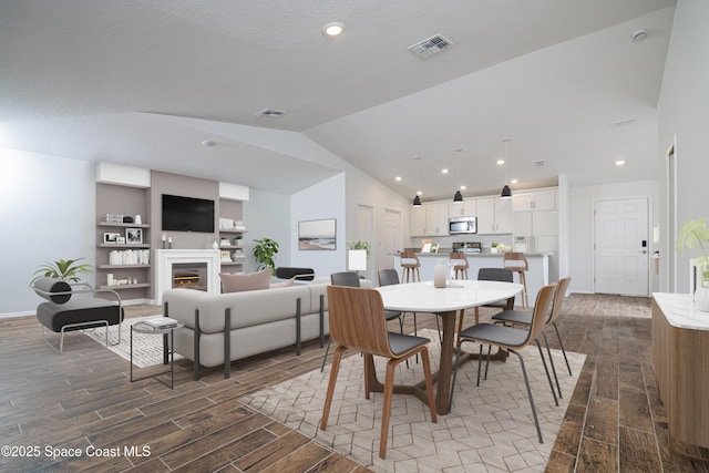 dining area with visible vents, a warm lit fireplace, wood finished floors, and vaulted ceiling
