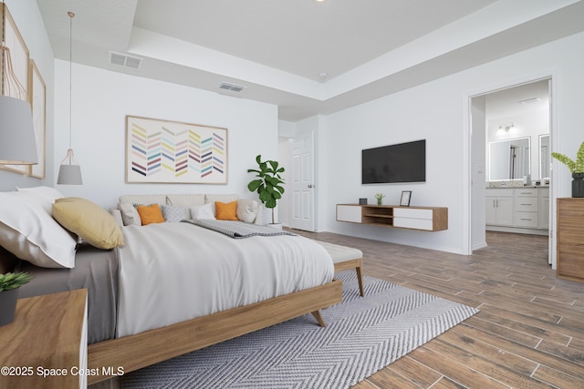 bedroom with ensuite bathroom, a tray ceiling, wood finished floors, and visible vents