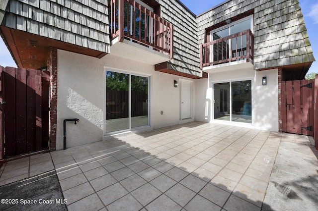 back of property featuring a gate, mansard roof, a balcony, a patio, and stucco siding