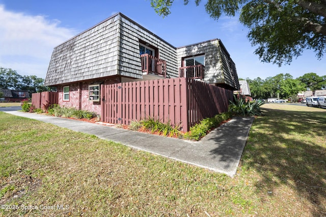 view of home's exterior featuring a yard, brick siding, mansard roof, and fence