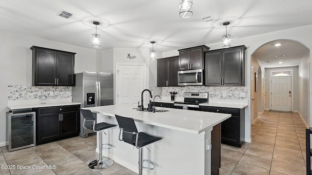 kitchen with appliances with stainless steel finishes, beverage cooler, arched walkways, backsplash, and a sink