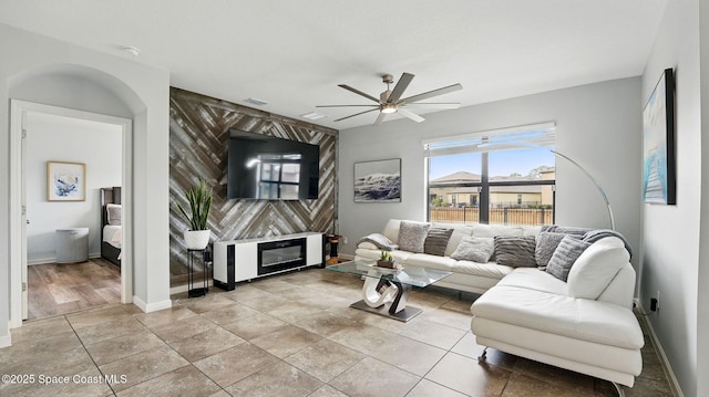 living room with an accent wall, ceiling fan, and baseboards