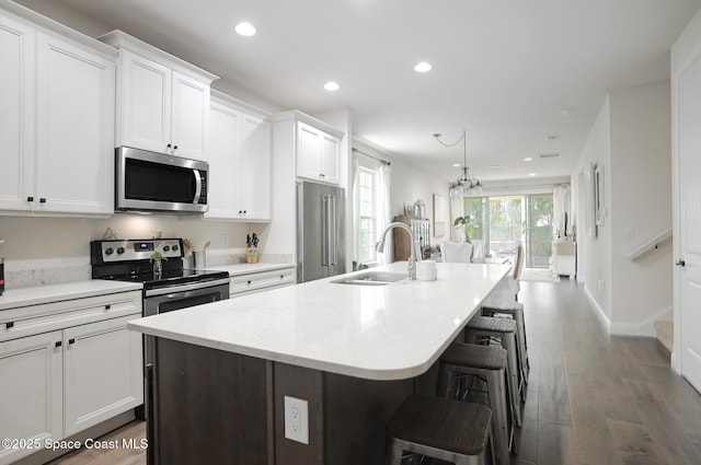 kitchen featuring a kitchen island with sink, recessed lighting, white cabinetry, a sink, and appliances with stainless steel finishes