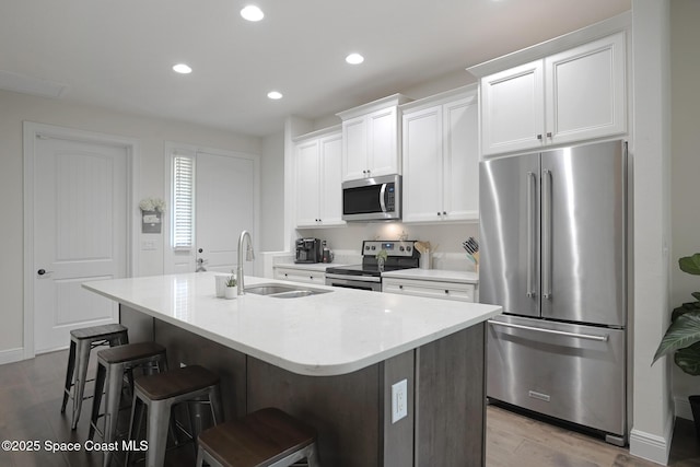 kitchen with an island with sink, a sink, appliances with stainless steel finishes, and wood finished floors