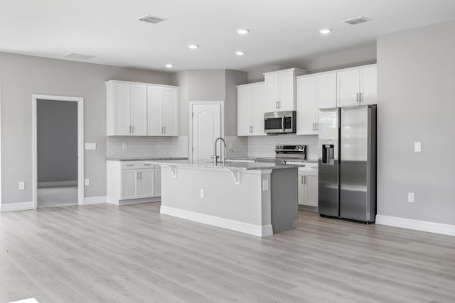 kitchen featuring visible vents, appliances with stainless steel finishes, a kitchen island with sink, and tasteful backsplash