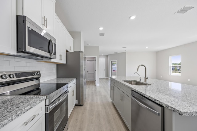 kitchen with visible vents, appliances with stainless steel finishes, a sink, light wood-style flooring, and an island with sink