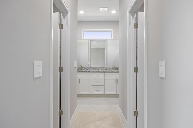 hallway with a sink, baseboards, and light colored carpet