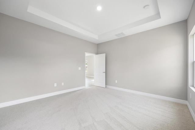 empty room featuring baseboards, light carpet, a tray ceiling, and visible vents