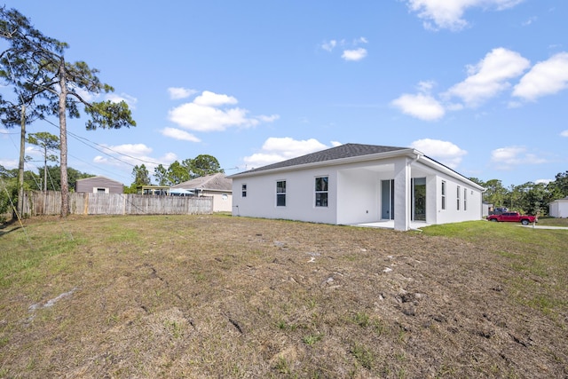 rear view of property with stucco siding, a lawn, and fence