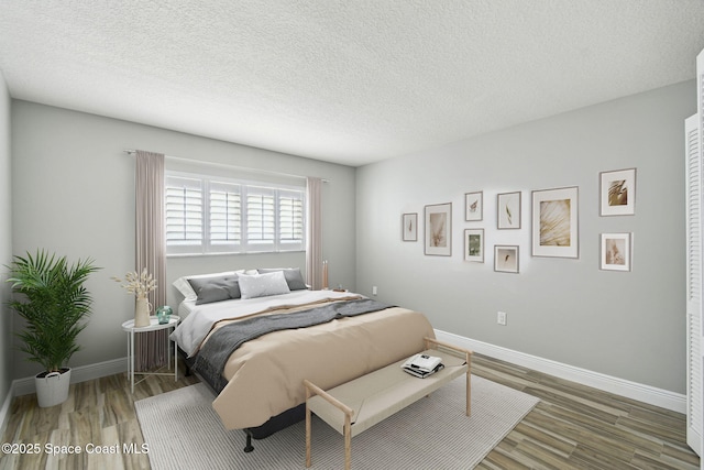 bedroom featuring baseboards, a textured ceiling, and wood finished floors