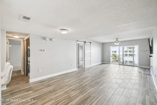 spare room featuring baseboards, light wood-style flooring, a ceiling fan, and a barn door